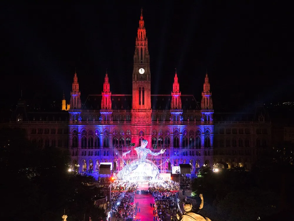 Rathaus bei Nacht, beleuchtet in Rot und Blau, große Figur vor dem Gebäude, Bühne mit Publikum