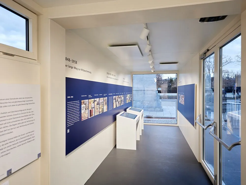 Ausstellung mit blauen Texttafeln, historischen Fotos und Touchscreens