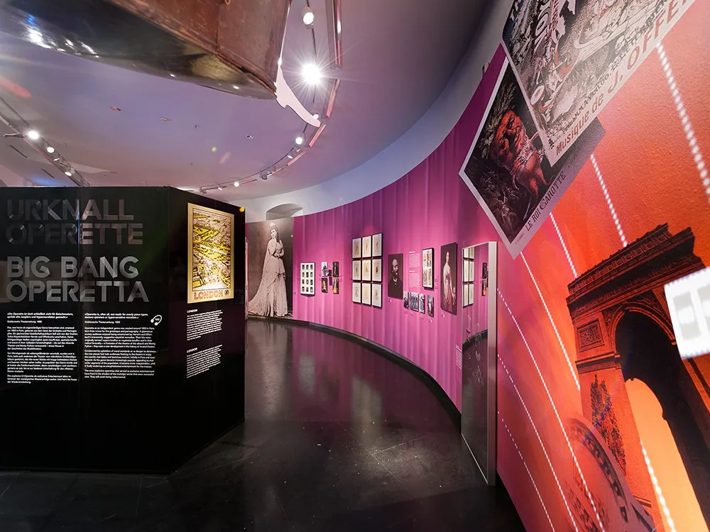 Ausstellungsraum: "Urknall Big Bang Operetta" mit Kunstwerken, historischen Fotos, Texten an einer rosa Wand