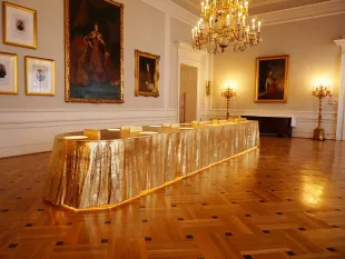 Langer goldener Tisch mit Struktur, große Gemälde historischer Personen an Wand