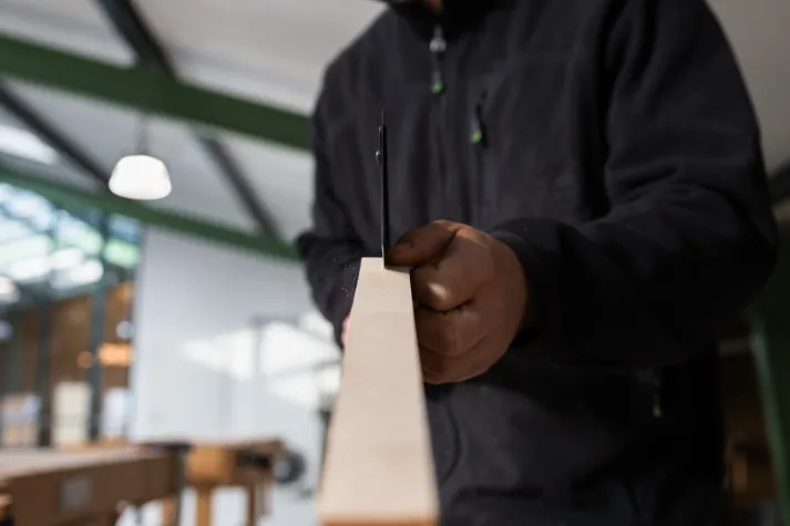 Person in einer dunklen Jacke sägt ein Holzbrett, aus einer nahen Frontperspektive aufgenommen