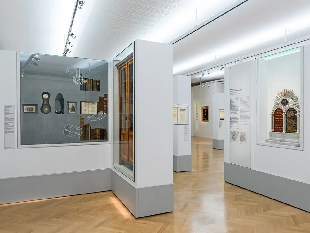 Ausstellungsraum mit Vitrinen, die historische Artefakten wie Büchern, einer Uhr und einem Davidstern-Dekor enthalten