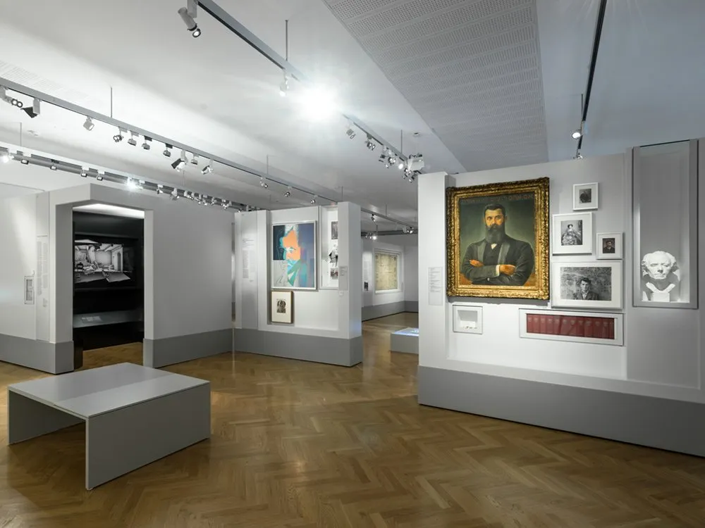 Ausstellungsraum, Vitrinen mit Gemälden und Artefakten, sowie einem grauen Tisch im Zentrum