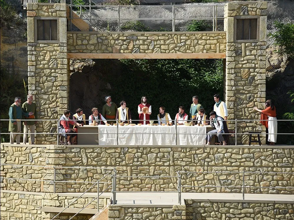 Szene des letzten Abendmahls, frontal aufgenommen aus der Ferne, zeigt Jesus in der Mitte, der das Brot teilt, umgeben von seinen Jüngern an einem langen Tisch mit Speisen.