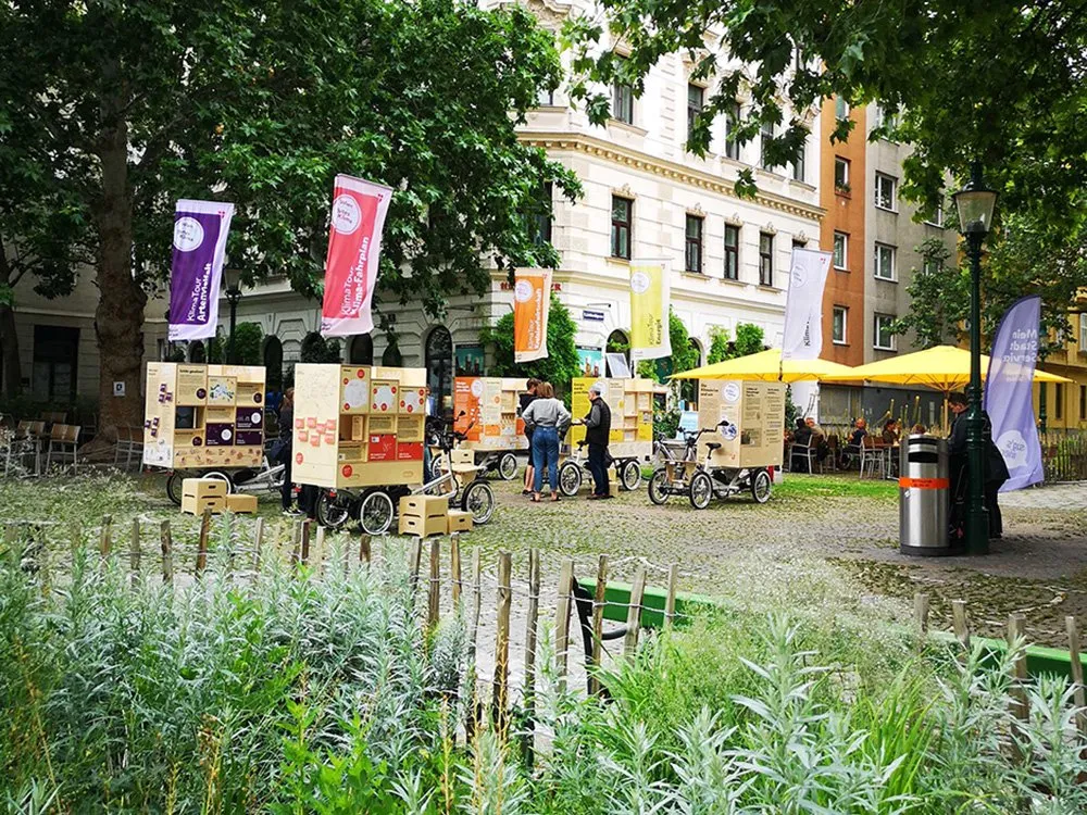 Begrünter Platz mit E-Lastenfahrrädern und Besuchern.