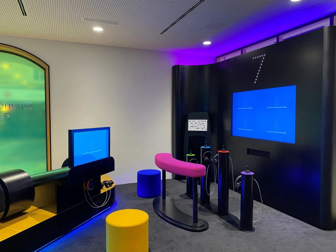Interaktive Station im FLiP Besucherzentrum mit Bildschirmen, bunten Sitzhockern und Bedienelementen