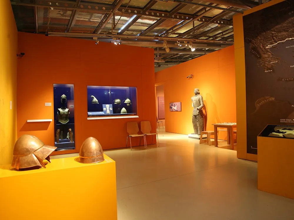 Ausstellungsraum: Vitrinen mit Teilen von Ritterrüstungen, orangene Wände