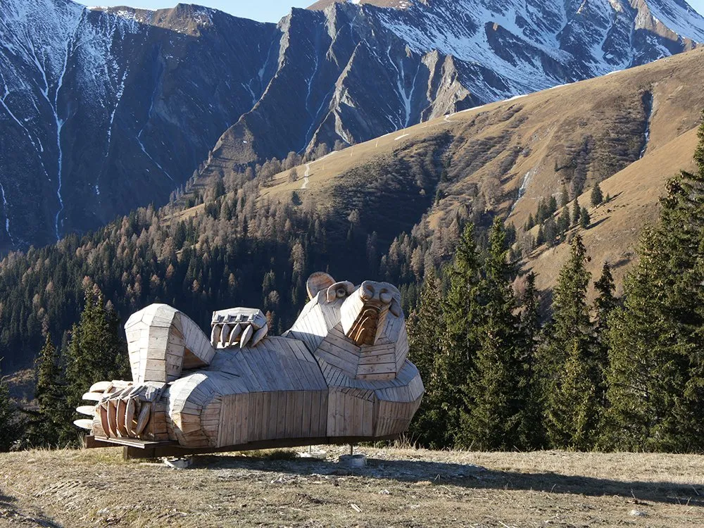 Liegende Bärenskulptur aus Holz in Berglandschaft