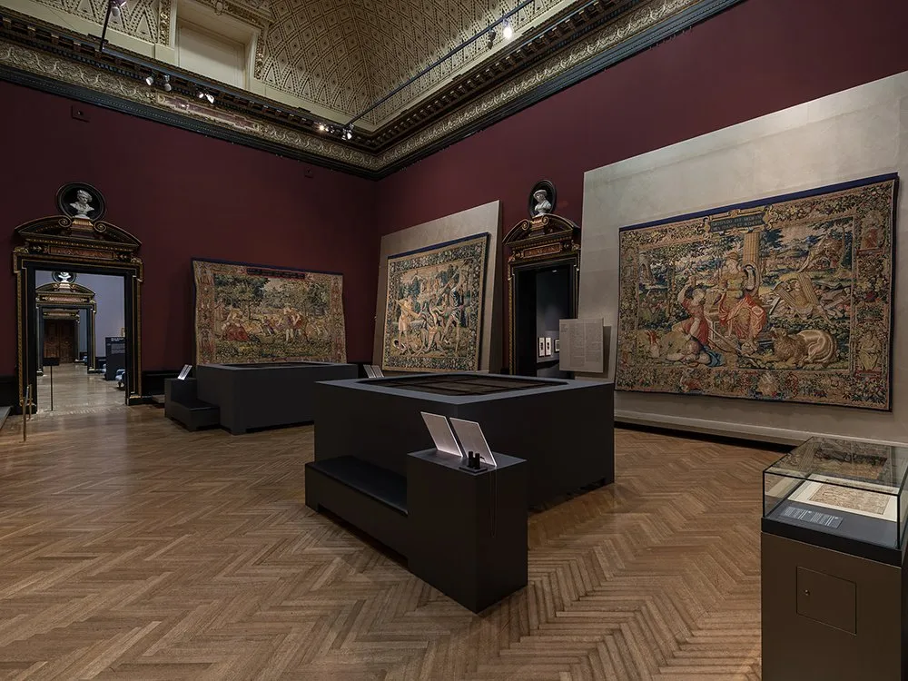 Ausstellungsraum: Gemälde an Wänden, schwarze Podeste mit Texten in Mitte