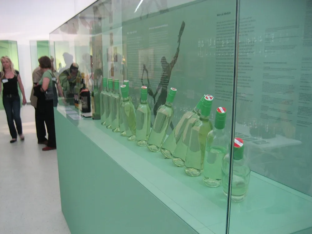 Vitrine mit vielen Weinflaschen, unterschiedlich positioniert mit Texten an Wand, Besucher im Hintergrund